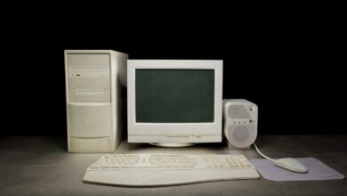 An old-school personal computer with a box-shaped monitor and a white keyboard. There is also a bulky speaker and mouse.