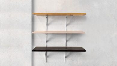 Three floating shelves are attached to a large white wall. Each shelf has a different shade of brown.