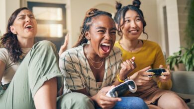 Three people sitting on a couch together and playing a video game on an unseen screen. All hold controllers.