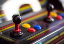 An arcade cabinet with two joy sticks and several buttons. The buttons are different colors.