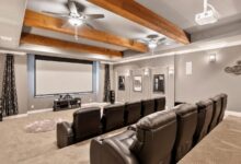 A home theater with two rows of recliners, a large screen, gray walls, and a ceiling decorated with wood beams and fans.