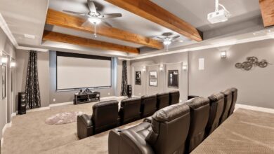 A home theater with two rows of recliners, a large screen, gray walls, and a ceiling decorated with wood beams and fans.