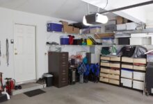 A home garage with white walls and multiple boxes, containers, and tools placed on the right side against the wall.